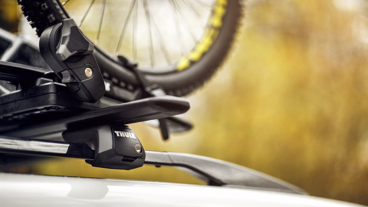 Detalle de la barra y el pie Thule sobre el techo de un vehículo, con bicicleta montada